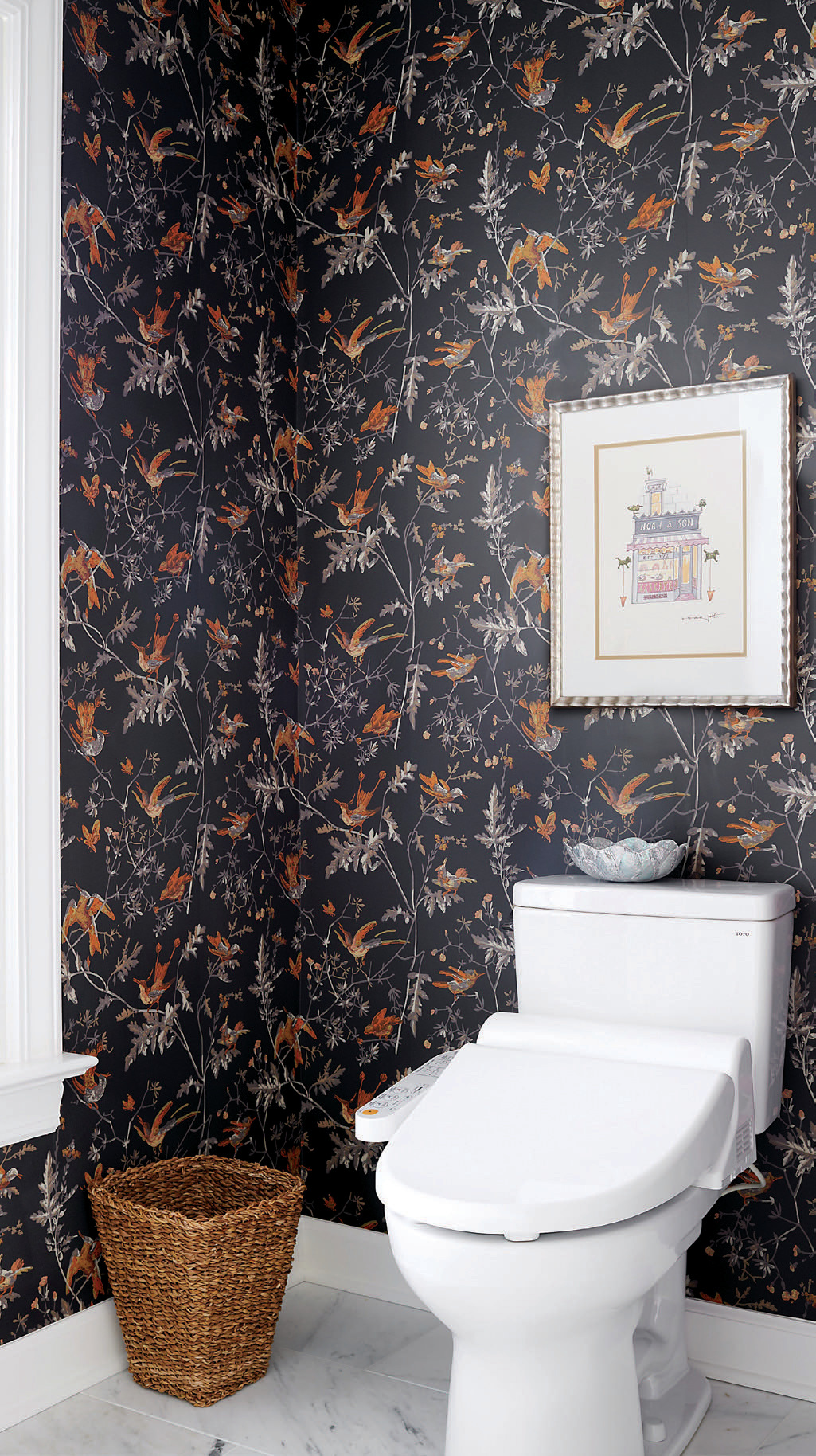 The water closet boasts bold décor, with dark-toned wallpaper that depicts the type of hummingbirds that often fly into the homeowners’ yard.
